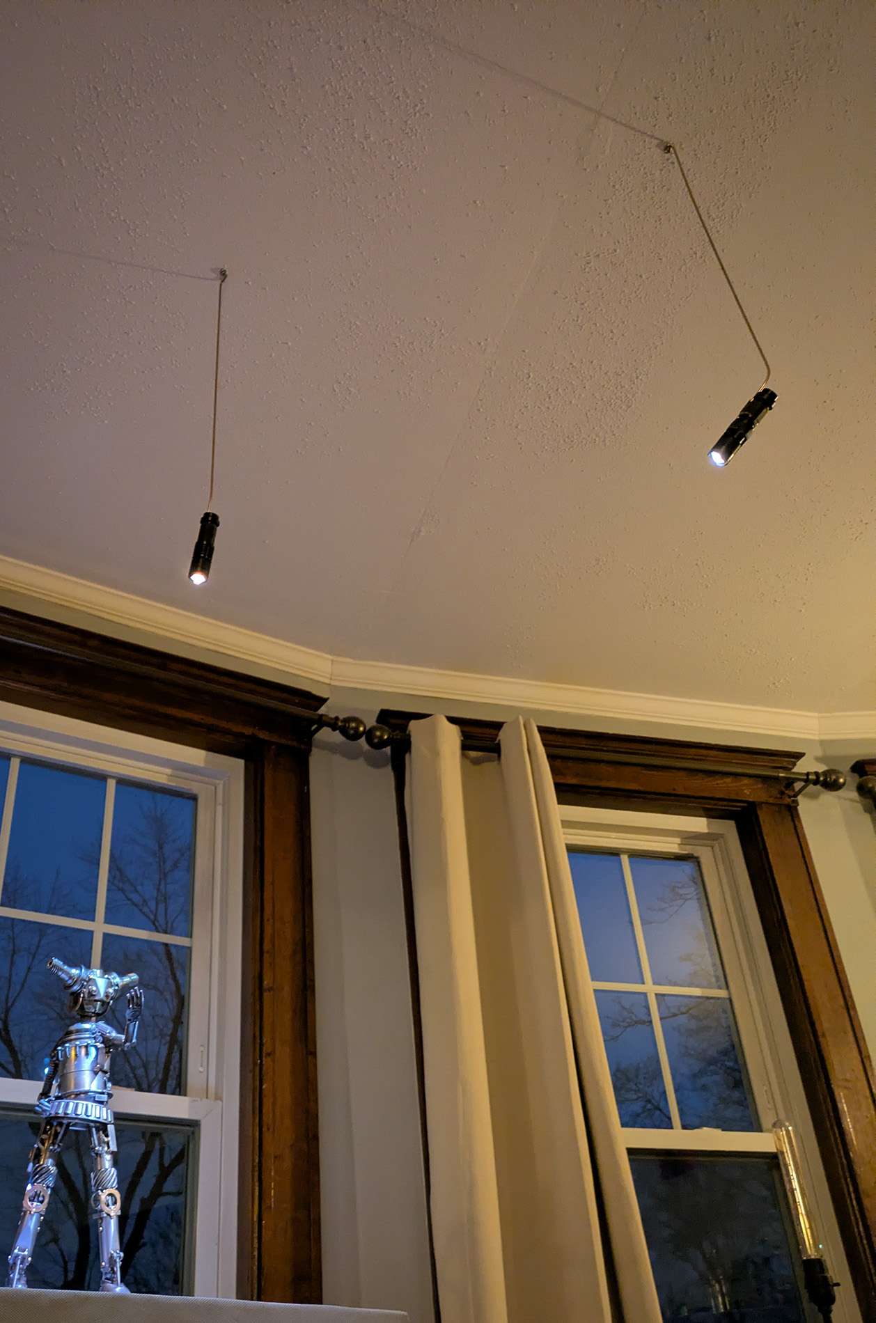 two LED flashlights taped to long bronze rods hang from the ceiling, illuminating a sculputre