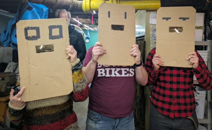 Three people hold up large cardboard masks with a single weld shied lens to look though